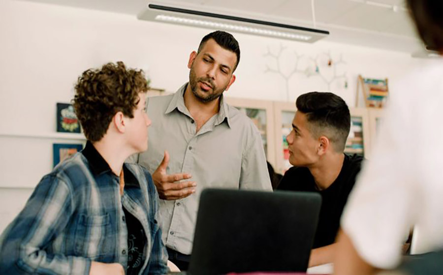 معلم در کلاس بزرگسال کنار دو دانش‌آموز نشسته و با آرامش به یکی می‌گوید اشکالی ندارد اگر اشتباه کنید، تا اعتماد به نفسش افزایش یابد