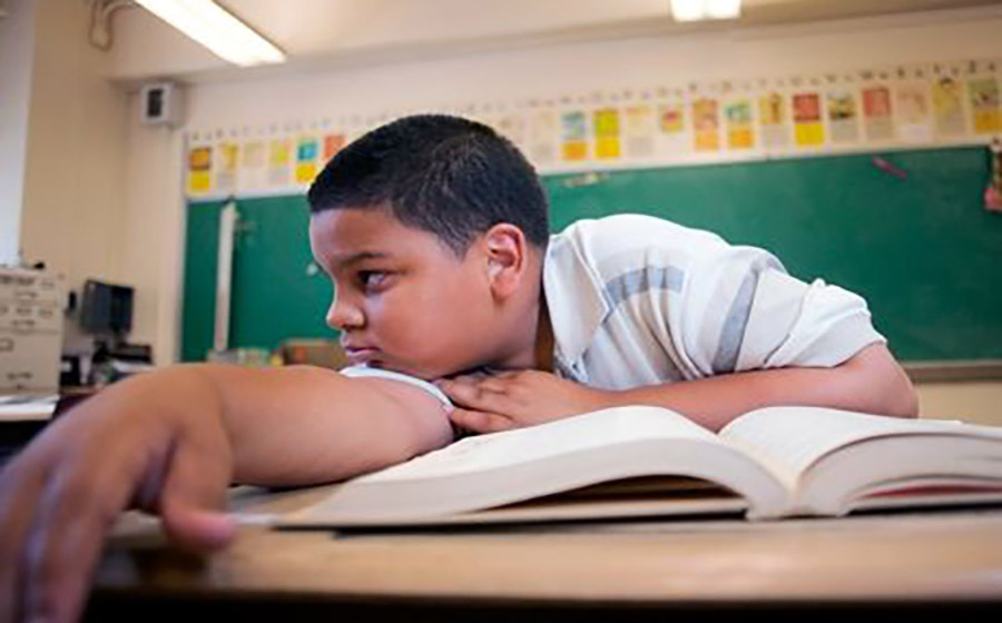 کودک ساکت و خجالتی که آرام در کلاس زبان نشسته و با نگاه پایین یا دست‌های گره‌خورده، نشانه‌هایی از اضطراب یا درون‌گرایی را نشان می‌دهد.