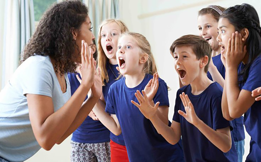 معلمی که همراه دانش‌آموزان در کلاس زبان با خنده و صدای بلند فریاد می‌زنند و در یک فعالیت شاد گروهی شرکت می‌کنند.