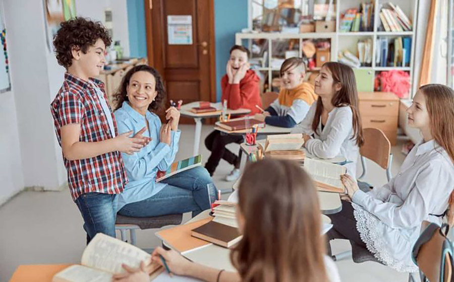 معلم در حال ارتباط صمیمی و لبخند زدن به کودکان در کلاس، نشان‌دهنده رابطه مثبت، حمایت هیجانی و تعامل مؤثر در محیط یادگیری.