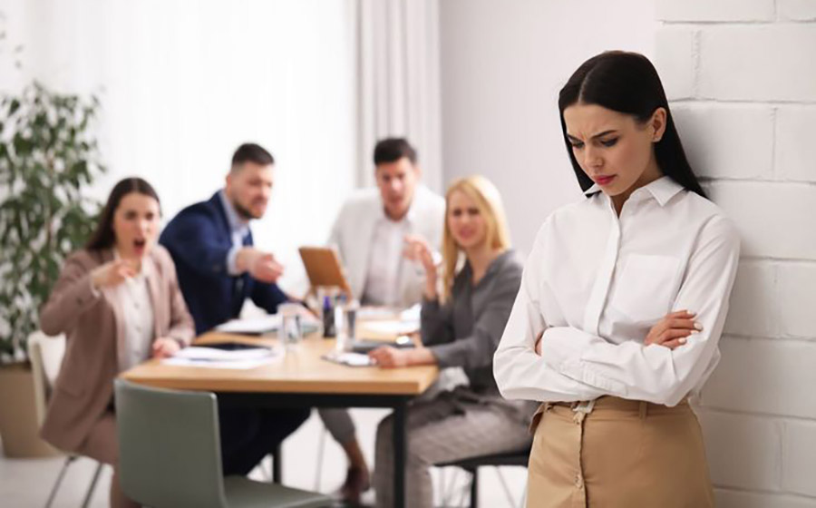 معلم خانم به دیوار تکیه داده، ناراحت و خسته، در حالی که همکارانش در حال صحبت یا تذکر دادن به او هستند، نشان‌دهنده فشار و چالش‌های مدیریت کلاس و تعامل با والدین.