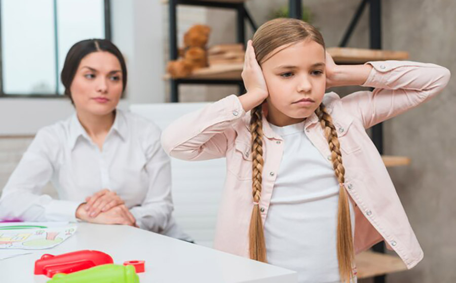 کودکی نشسته و گوش‌های خود را گرفته، و معلم با چهره‌ای بی‌احساس نگاه می‌کند—نمادی از سوءتفاهم میان لجبازی و اضطراب کودک.