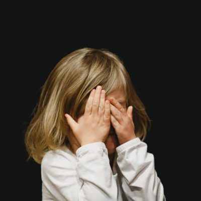 کودک در تاریکی با دستان روی صورت، نشاندهنده اضطراب، ناراحتی یا نیاز به حمایت و مراقبت؛ نمادی از کودک درون و اهمیت توجه به احساسات درونی.