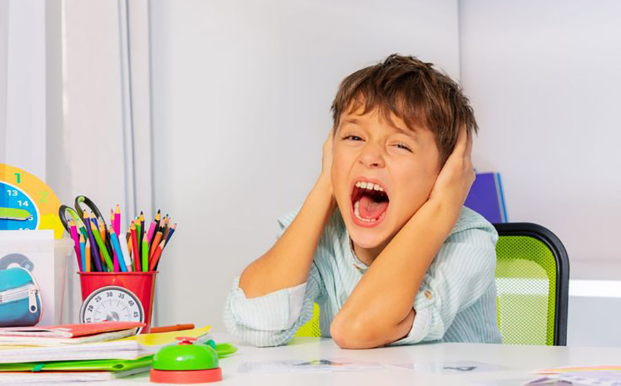 کودکی که در کلاس زبان پشت میز نشسته و با داد زدن و پرخاشگری نشان می‌دهد، در حالی که مداد رنگی و وسایل نقاشی روی میز و اطرافش قرار دارند، به مدیریت رفتار و هیجانات نیاز دارد.