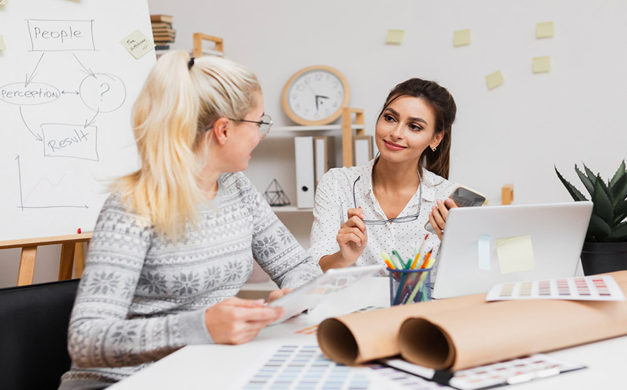 دو معلم در فضای مدرسه کنار هم هستند و در حال گفت‌وگویی صمیمی هستند؛ یکی با لبخند گوش می‌دهد و دیگری با دست حرف می‌زند. حس نزدیکی، همدلی و صحبت حرفه‌ای بینشان دیده می‌شود.